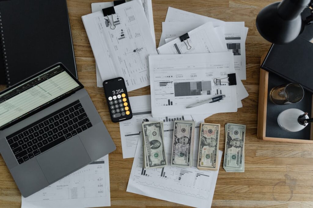 A imagem mostra várias planilhas, dinheiro, notebook e um celular sobre a mesa para planejar a gestão financeira para nômades digitais.