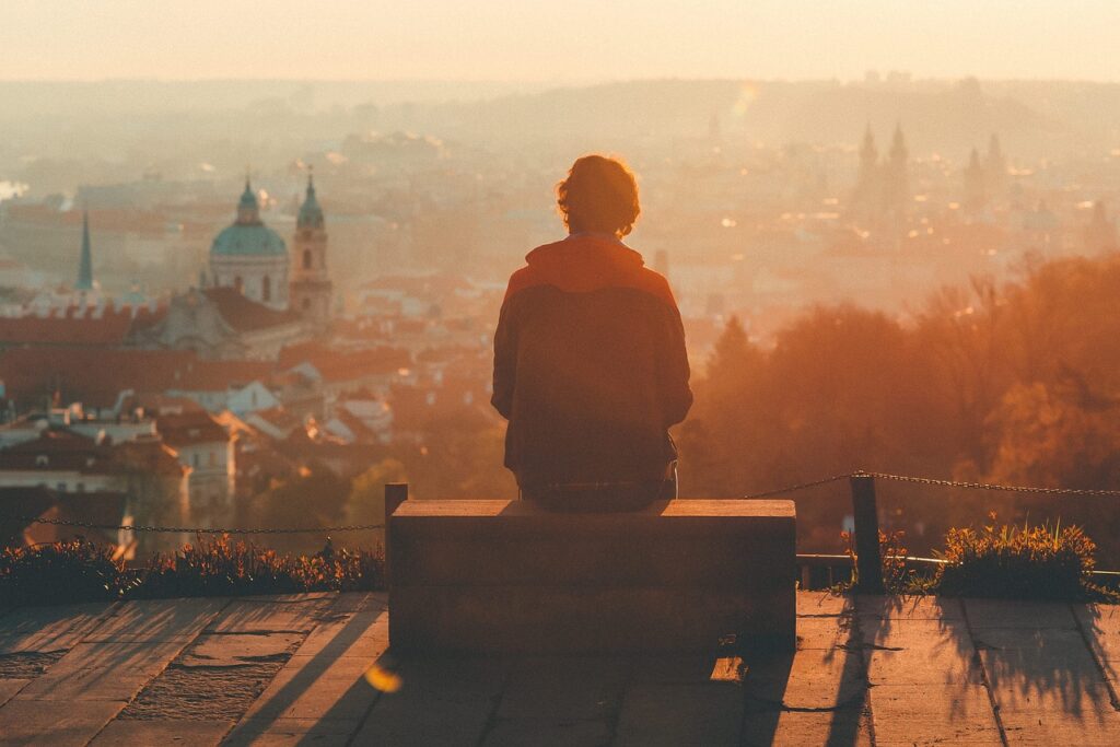 A imagem mostra uma mulher sentada sozinha admirando a paisagem de uma cidade, reforçando a importância da atenção para a solidão na vida nômade.